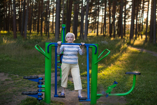 Very elderly woman doing morning exercise on the street sport playground. - Foto, Bild