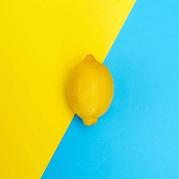Ένα κίτρινο λεμόνι σε κίτρινο-μπλε φόντο. Η θέα από την κορυφή. - Φωτογραφία, εικόνα