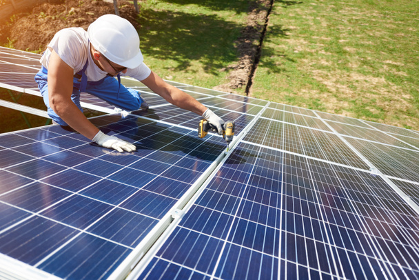 Professional worker installing solar panels on the green metal construction, using different equipment, wearing helmet. Innovative solution for energy solving. Use renewable resources. Green energy. - Photo, Image