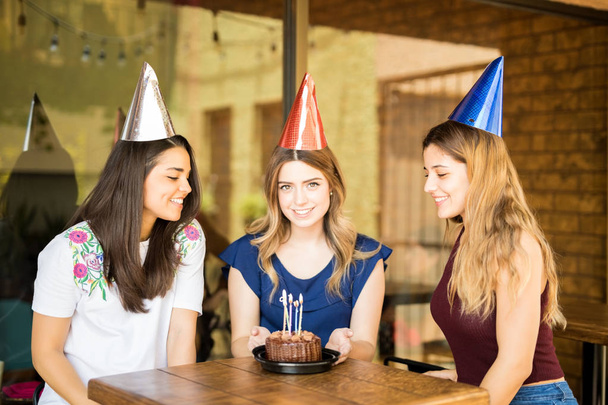 Beautiful young woman wearing party hats celebrating her birthday with friends in a restaurant - Photo, Image