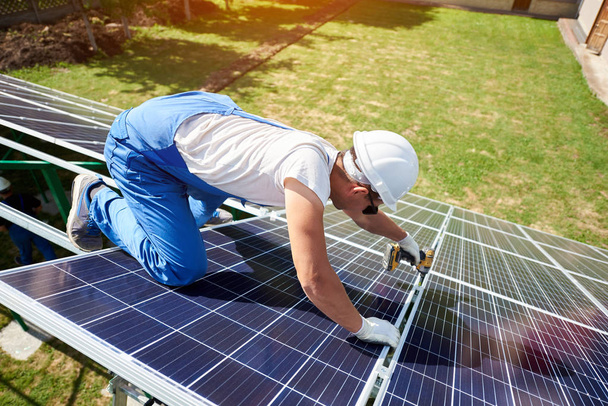 Professional worker installing solar panels on the green metal construction, using different equipment, wearing helmet. Innovative solution for energy solving. Use renewable resources. Green energy. - Foto, imagen