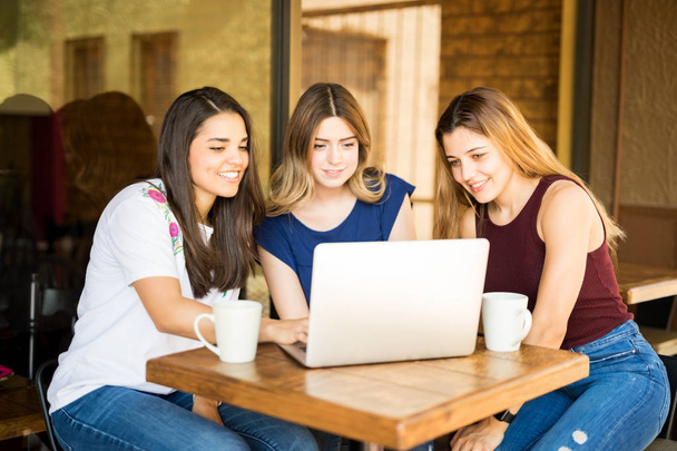 Three young woman looking at laptop computer and smiling at coffee sho - Zdjęcie, obraz