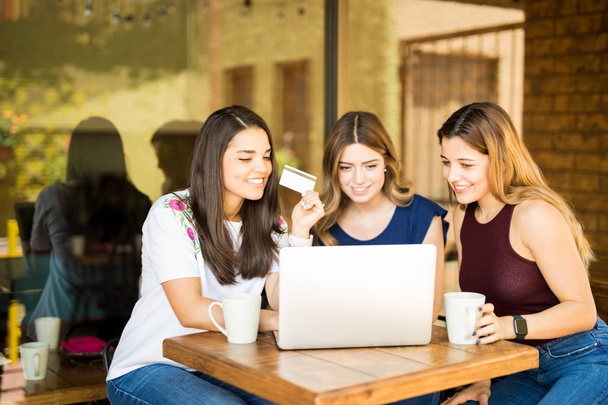 Skupina mladých žen pomocí přenosného počítače s kreditní kartou v ruce, dělá online nakupování u restaurace - Fotografie, Obrázek