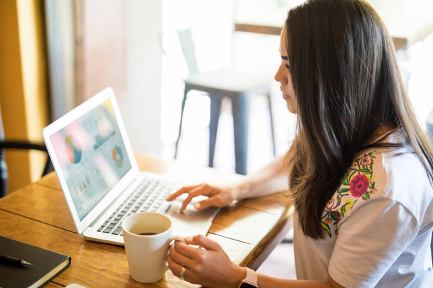 Jeune femme d'affaires faisant une présentation financière sur son ordinateur portable et prenant un café à caf
 - Photo, image
