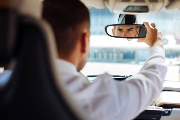 Serious smart man fixing the rearview mirror - 写真・画像