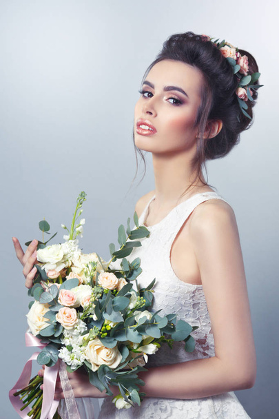 Spring beauty portrait of sexy bride with hairstyle, wreath and bouquet in hands on gray background. - Фото, изображение