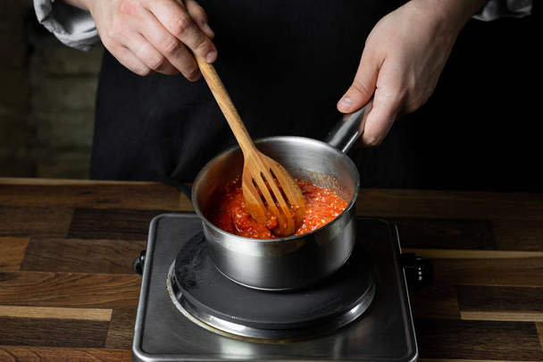 Cooking tomato sauce in metal saucepan by chef hands, steps process on kitchen on black background copy text recipe. - Fotografie, Obrázek