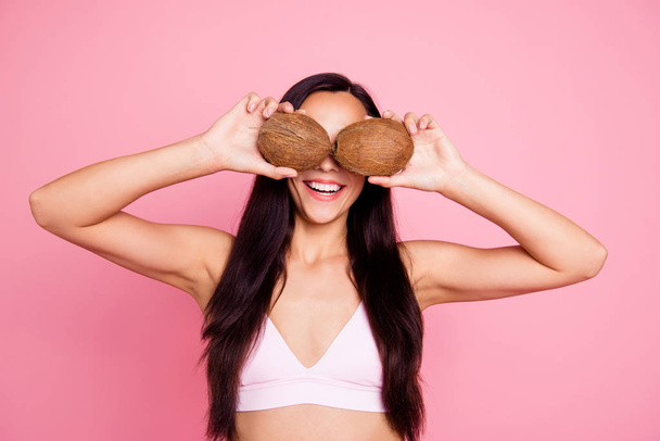 Big staring pop eyes concept. Close up studio photo portrait of pretty cute with long straight brunette brown hair lady with beaming toothy smile holding coconuts isolated on pastel bright background - Фото, изображение
