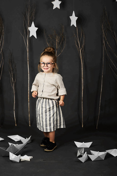 little girl with glasses on grey background with stars, trees and paper boats - Foto, Imagen