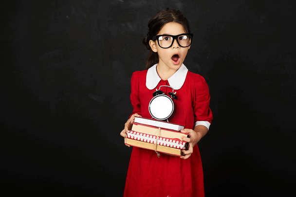 schoolgirl in a red dress with a books and clock on a black background  - Foto, immagini