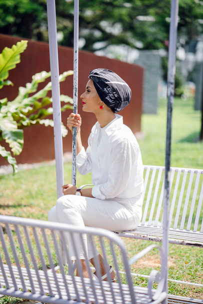 Portrait of a young Muslim woman wearing a turban (headscarf, hijab). She is sitting on swing - Φωτογραφία, εικόνα