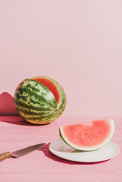 close up view of slice of watermelon on plate and knife on pink background - Foto, Imagen