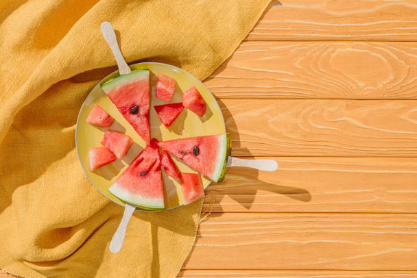 flat lay with watermelons on ice cream sticks on plate on wooden tabletop with linen - Foto, Bild