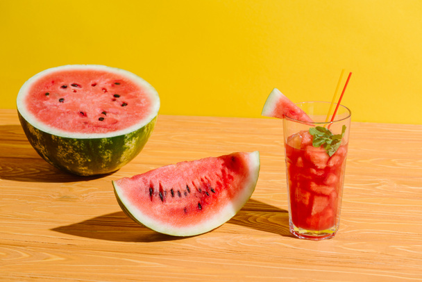 close up view of fresh watermelon and watermelon drink in glass on wooden surface on yellow background - Photo, Image