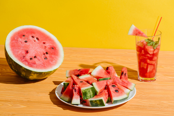 close up view of fresh watermelon pieces and watermelon drink in glass on wooden surface on yellow background - Photo, Image