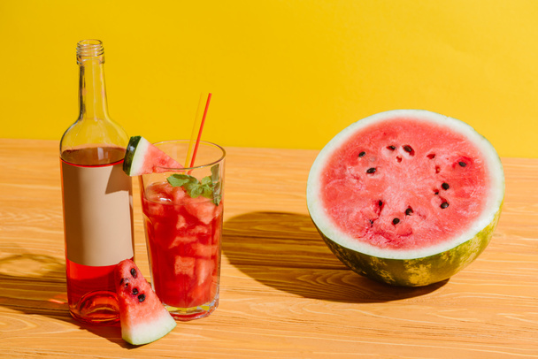 Nahaufnahme von frischer Wassermelone und Wassermelonengetränk auf Holzoberfläche auf gelbem Hintergrund - Foto, Bild