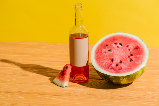 close up view of fresh watermelon and watermelon drink in bottle on wooden surface on yellow background - Fotó, kép