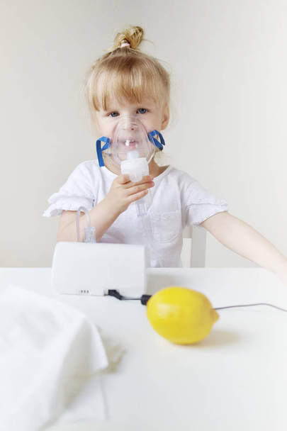 Pieni tyttö hengityssuojaimessa, jolloin sisäänhengitys sumuttimella kotona inhalaattori pöydällä, sisätiloissa, sairas lapsi
 - Valokuva, kuva