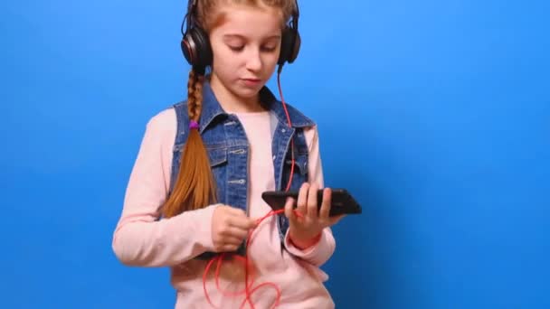 A little girl connects the headphones to the phone and enjoys the music - Filmati, video