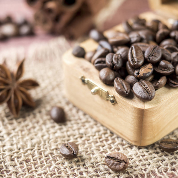 Coffee beans in a wooden box with cinnamon sticks and star anise on burlap napkins. - Photo, Image
