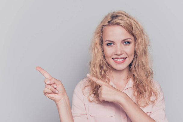 Attractive cute curly-haired blonde gorgeous caucasian charming young smiling girl wearing formal wear shirt pointing fingers. Copy space. Isolated over grey background - Valokuva, kuva