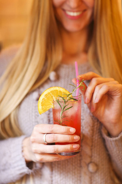 Young pretty woman with red cocktail decorated with rosemary and orange. Close up - Valokuva, kuva