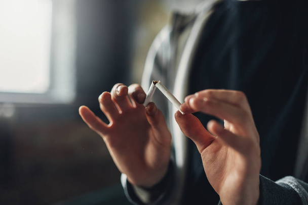 Addicted male person breaks a cigarette, blur background. Smoking addiction concept - Zdjęcie, obraz