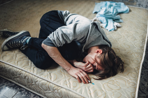 Чоловічий наркоман з шприцом в руці спить в ліжку після дози. Концепція наркоманії, наркоманії
 - Фото, зображення