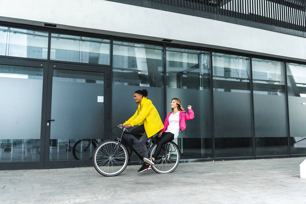 счастливая мультикультурная пара на велосипеде на городской улице
 - Фото, изображение