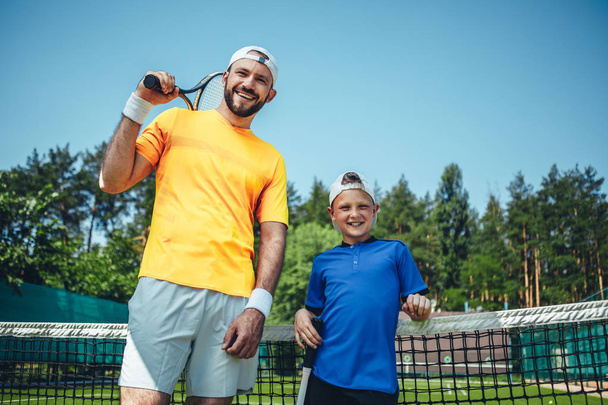Positive man and boy holding tennis rackets - Photo, image