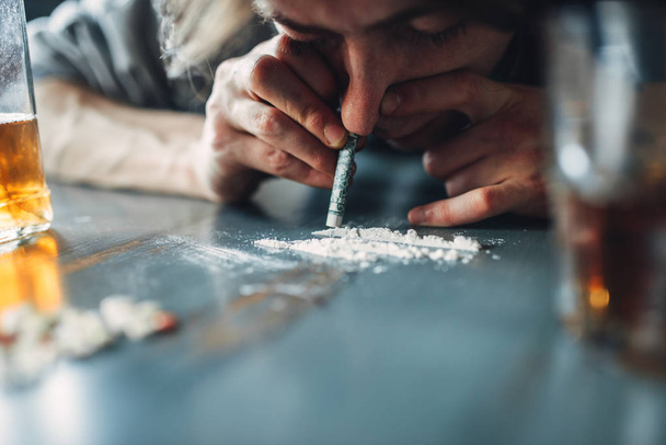 Wąchania linię, kokaina, narkotyki i butelkę alkoholu na stole na tle płci męskiej junkie. Uzależnienie od koncepcji, osób uzależnionych - Zdjęcie, obraz