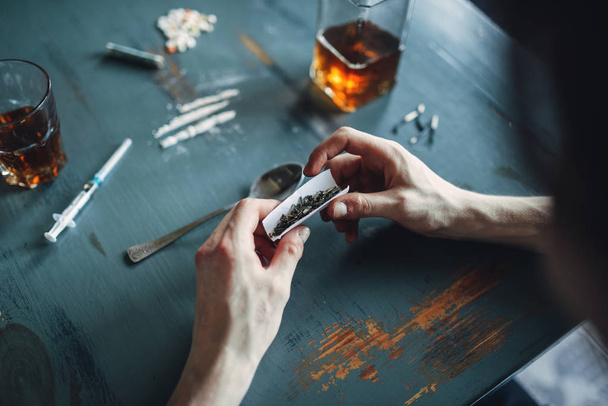 Narkotyków nałogowiec ręce przygotowuje dawki, widok z góry, butelkę alkoholu i strzykawek na stole na tle. Koncepcja narkotyczne uzależnienie, osób uzależnionych, junkie - Zdjęcie, obraz