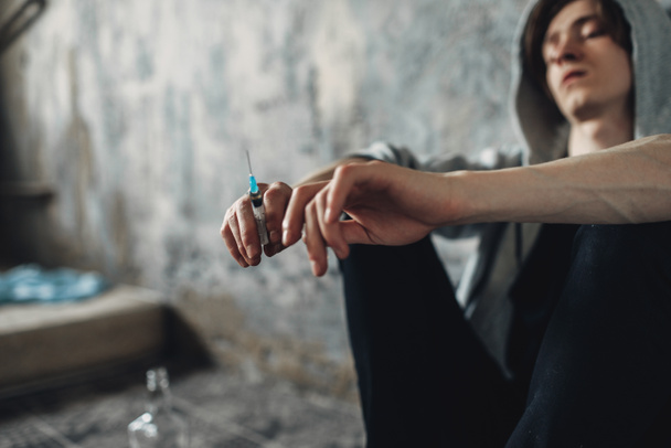 Джункі з шприцом в руці, що сидить на підлозі після дози, пляшка алкоголю поруч. Концепція наркоманії, наркоманії
 - Фото, зображення