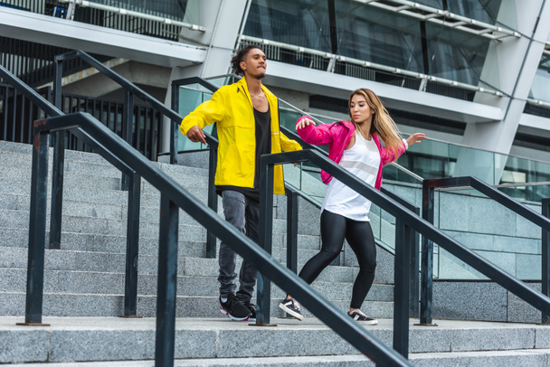 junges multiethnisches Paar tanzt auf der Treppe einer städtischen Straße - Foto, Bild