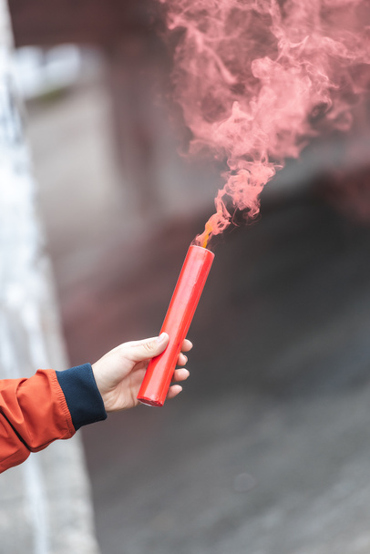 bijgesneden afbeelding van een jonge vrouw met rode rookbom bij city straat - Foto, afbeelding