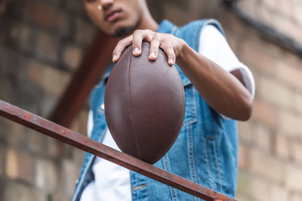 selective focus of american football ball in hand of young man at street - Foto, afbeelding
