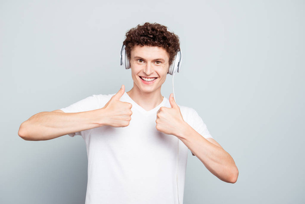 Portrait of brunet guy in big white headphones shows thumbs up isolated on light gray background - Valokuva, kuva