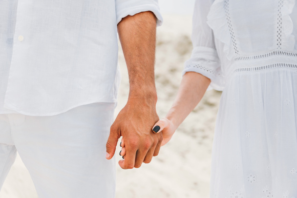 Schnappschuss von Paar in Weiß, das Händchen haltend vor Sanddüne - Foto, Bild
