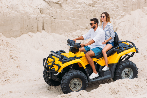 beautiful young couple riding yellow all-terrain vehicle in desert - Photo, Image