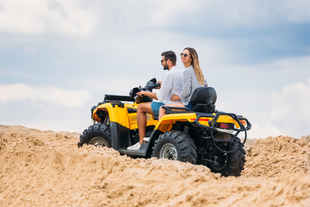 active young couple riding all-terrain vehicle in desert on cloudy day - Фото, зображення
