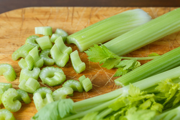 Čerstvý celer nakrájíme na malé kousky na dřevěné desce - Fotografie, Obrázek