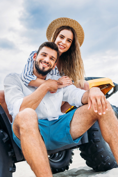 vista inferior de feliz jovem casal sentado no ATV na frente do céu nublado
 - Foto, Imagem