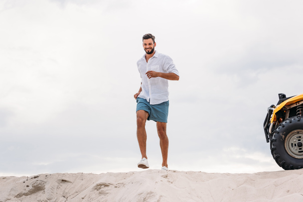 jovem atraente correndo na duna de areia na frente do céu nublado
 - Foto, Imagem