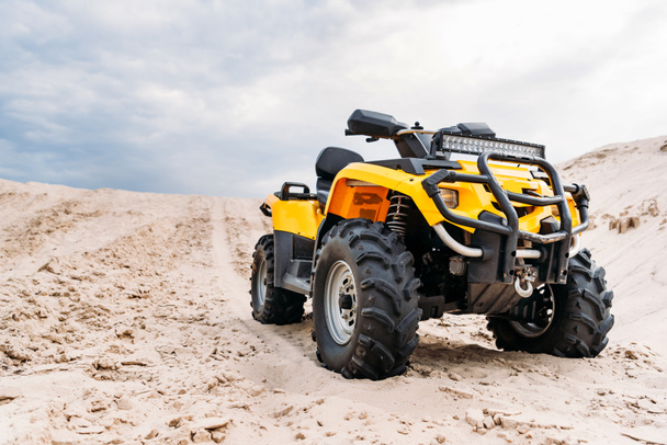 bottom view of modern yellow all-terrain vehicle standing in desert on cloudy day - Foto, afbeelding