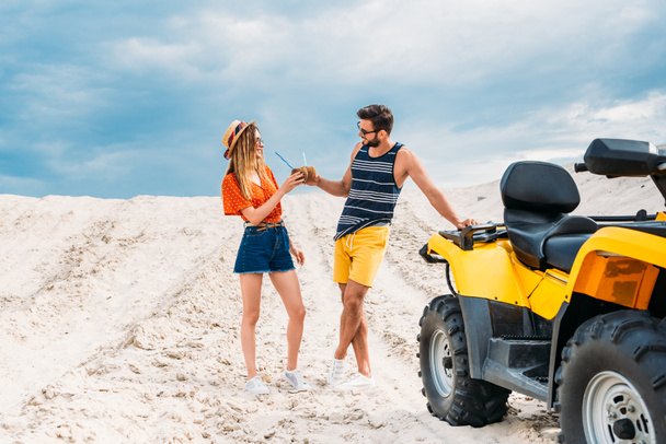 relaxed young couple with atv and coconut cocktails in desert - Foto, Imagem