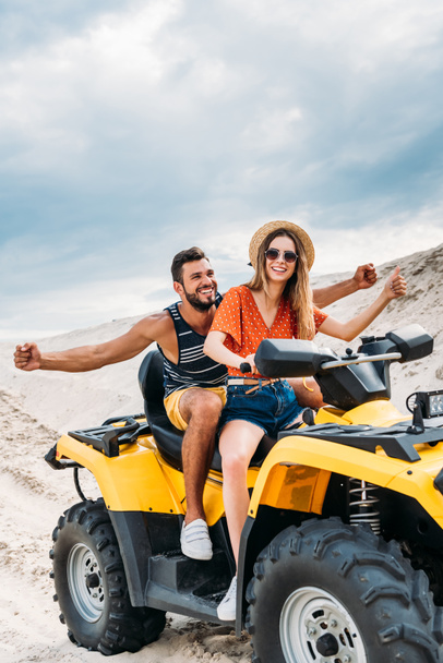 happy young couple riding all-terrain vehicle in desert on cloudy day - Zdjęcie, obraz
