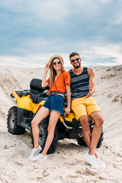 beautiful young couple leaning back on ATV in desert - Zdjęcie, obraz