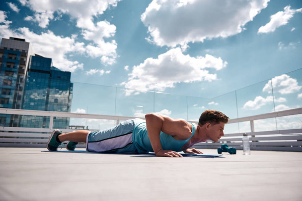 Athlete is doing push-ups on sunny terrace - Фото, изображение
