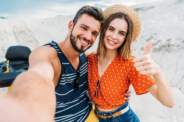 point of view of shot of young couple taking selfie and showing thumb up in desert - Photo, Image