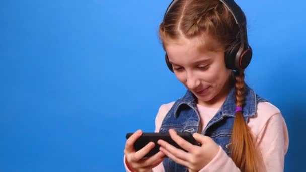 Little girl in headphones playing the video game on her smartphone - Záběry, video